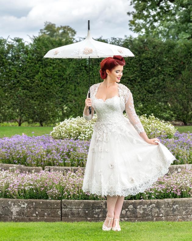 Bride poses in manicured gardens with parasol by Shoe Design and Bridal by J