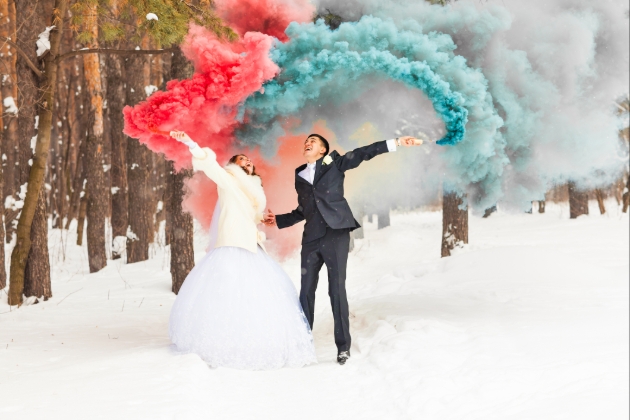 Couple wave coloured smoke bombs in snowy woodlands