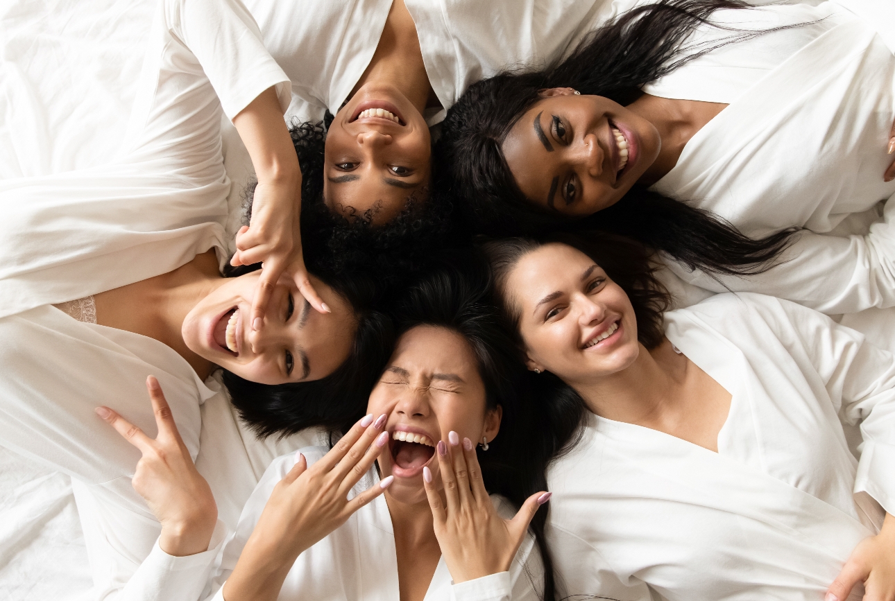 Group of bridesmaids in white dressing gowns lie on a bed
