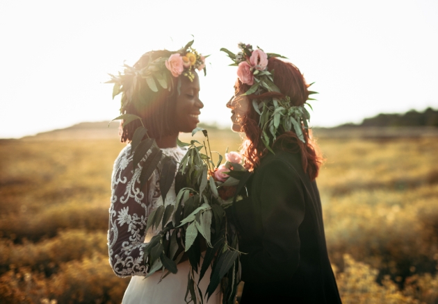 two women in wedding outfits holding hands at sunset in a field