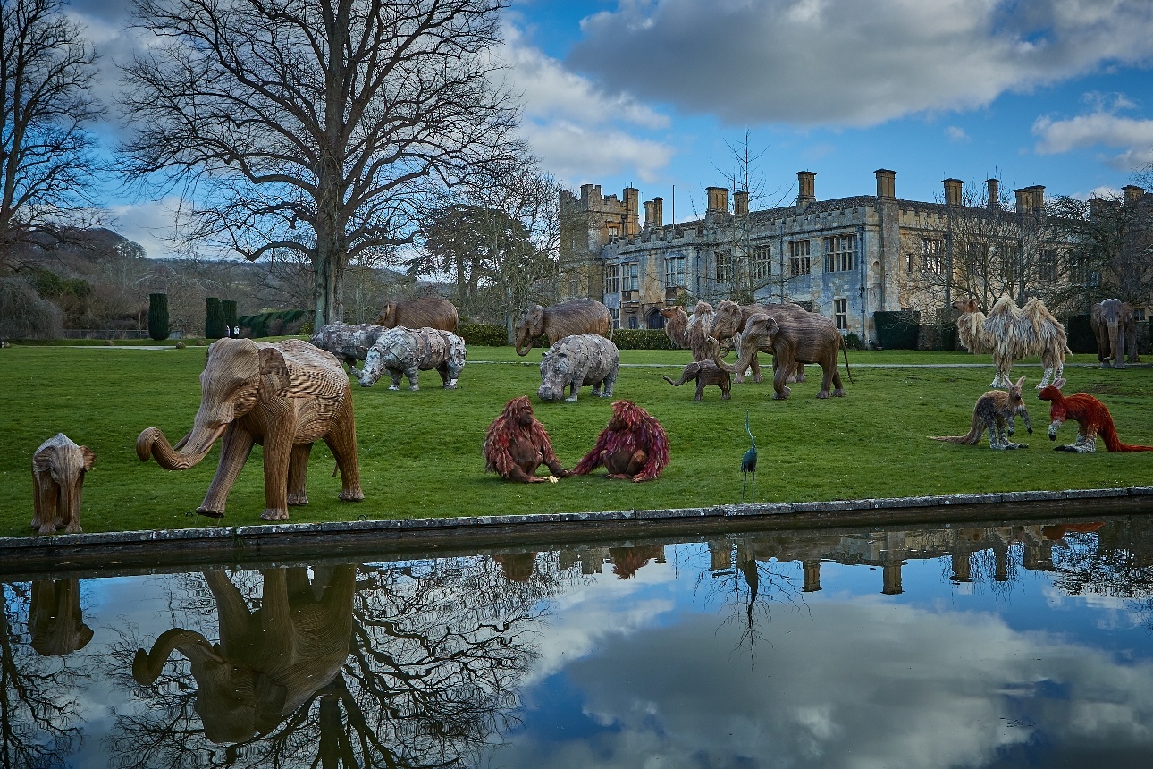 castle in the background with large animal statues around the grass and by the water