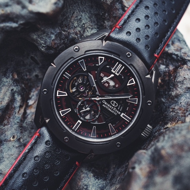 A close up of a black watch with a black leather strap and red stitching